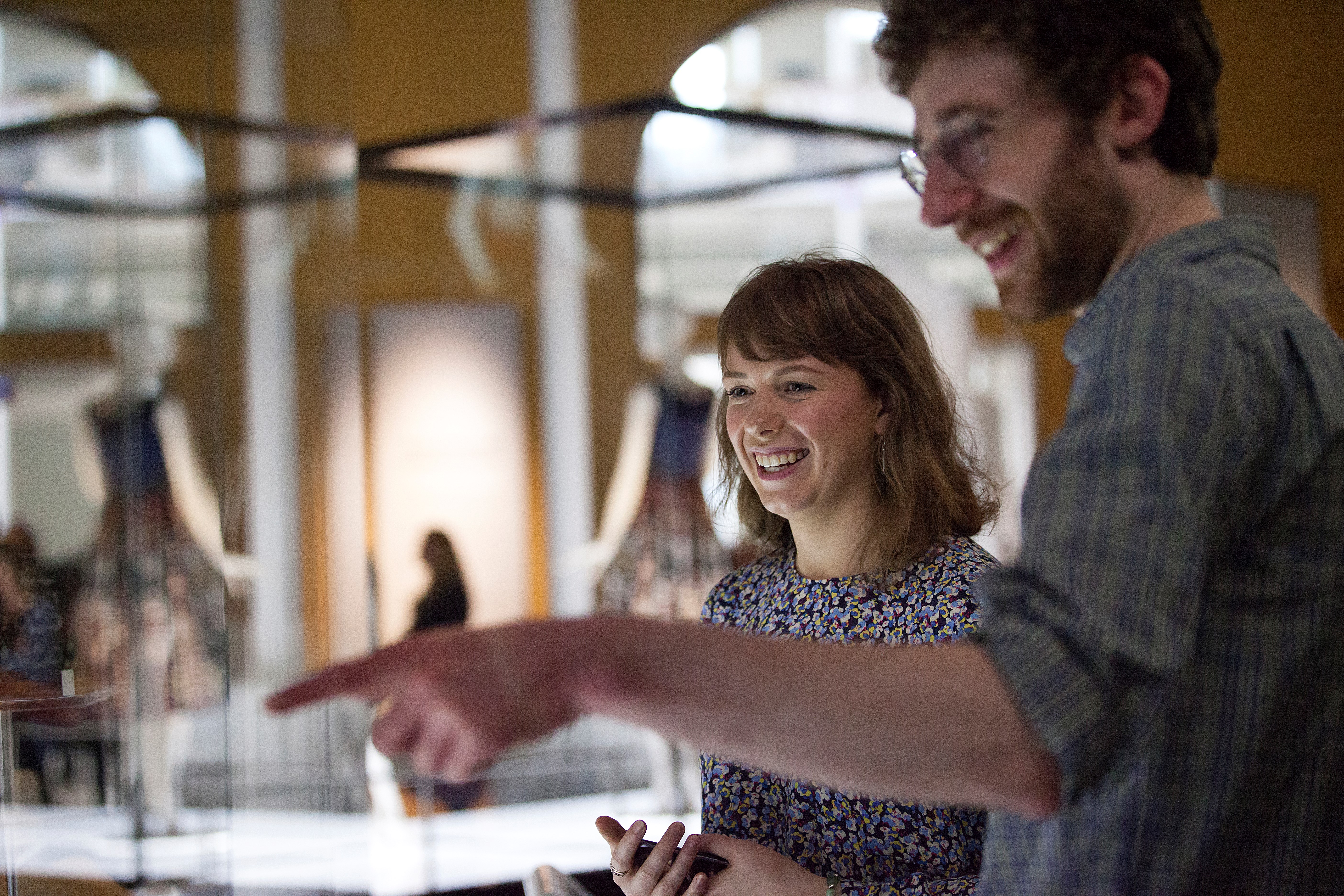 Woman and man smiling in a gallery with glass cases out of focus..