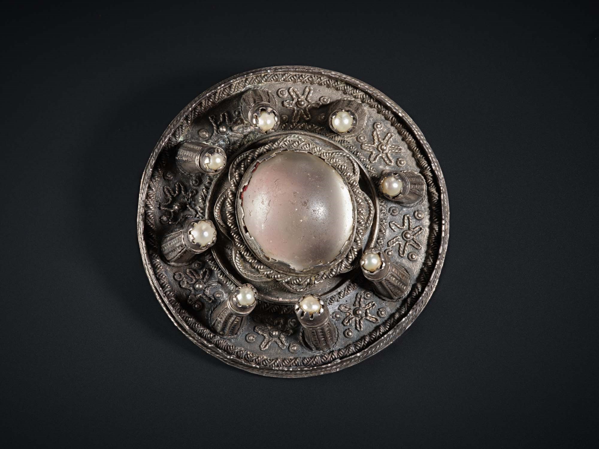 A circular metal brooch with raised decorative elements.
