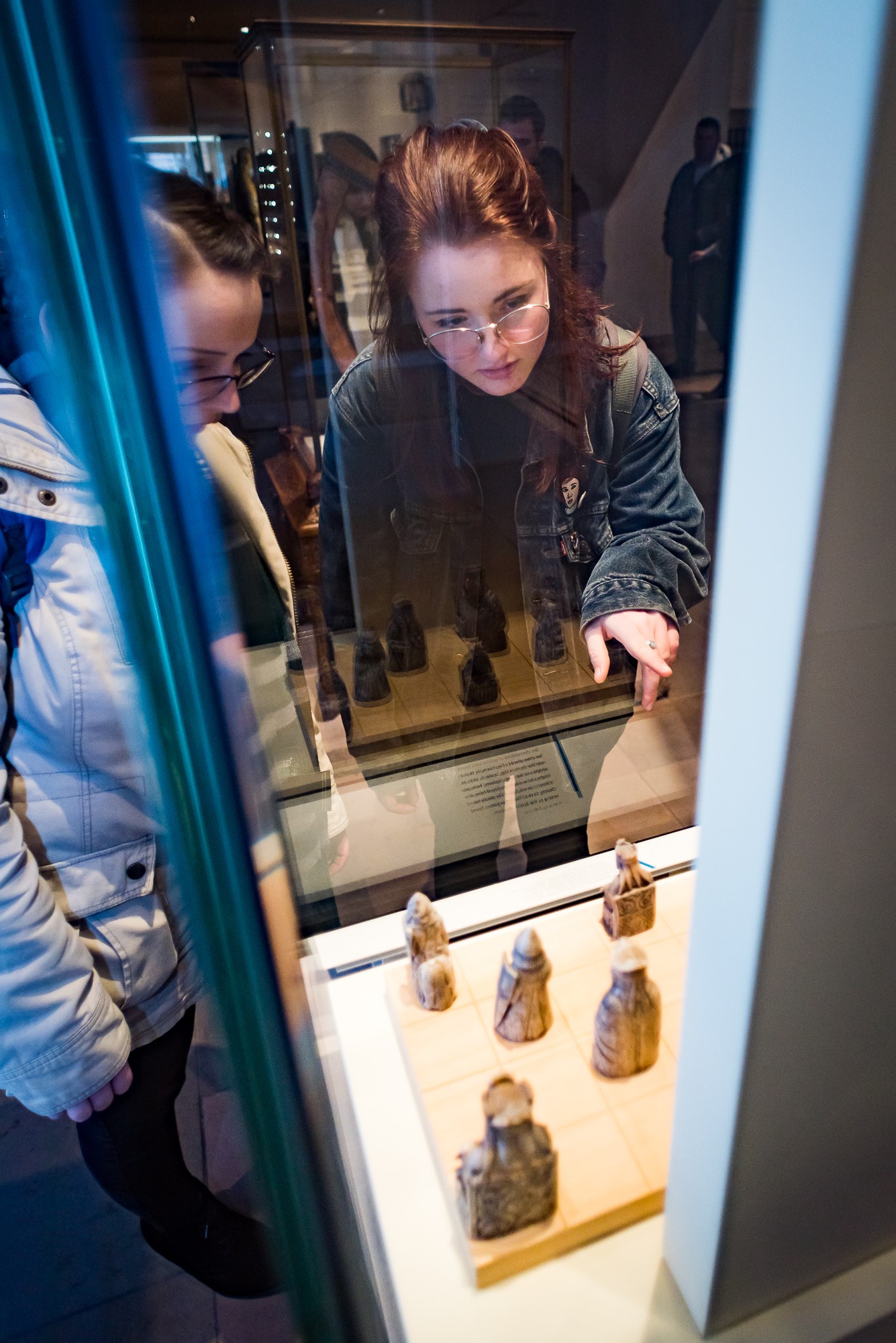 Two visitors looking at Lewis chess pieces in a glass cabinet.