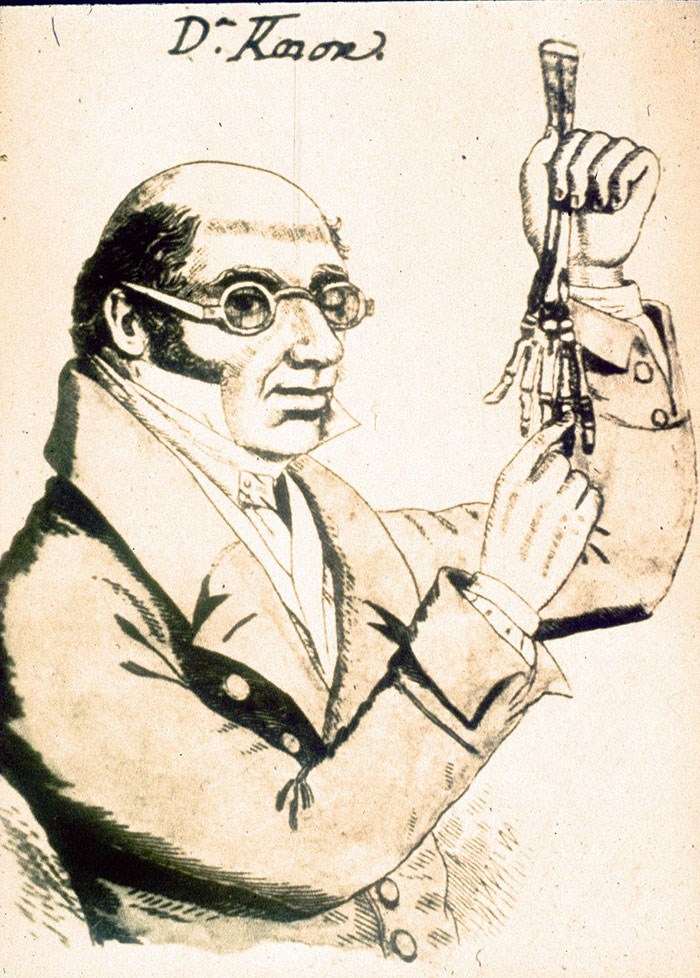 Sketch of a man in a collared suit and small goggles holding up a skeletal human hand and lower arm.