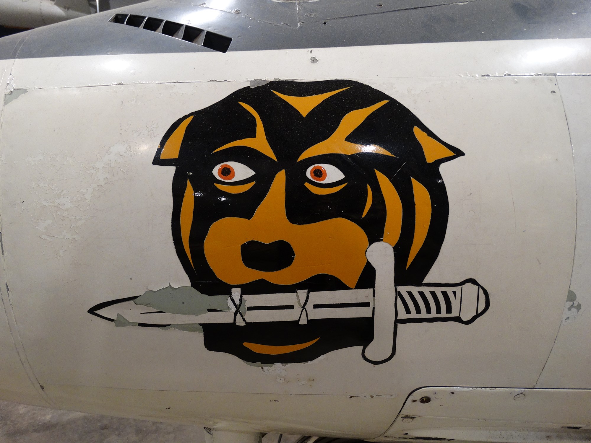 The side of a plane with a dog holding a knife in its mouth painted on it