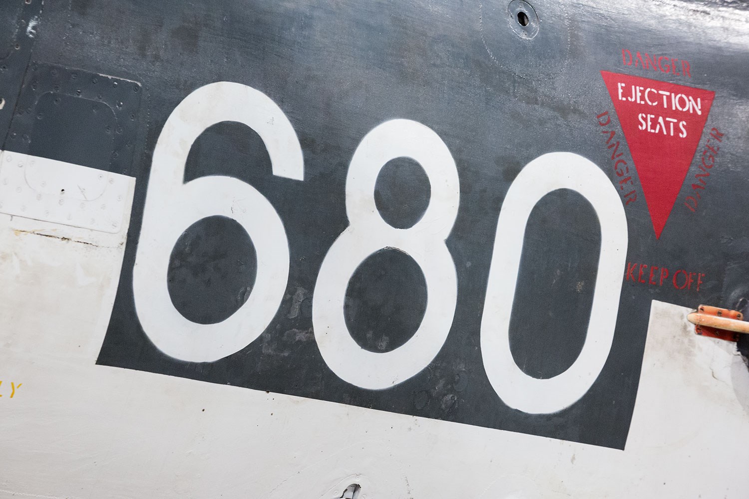 The side of a Sea Venom aircraft. There is the number 680 painted on the side and a symbol of a red triangle for ejection seats.