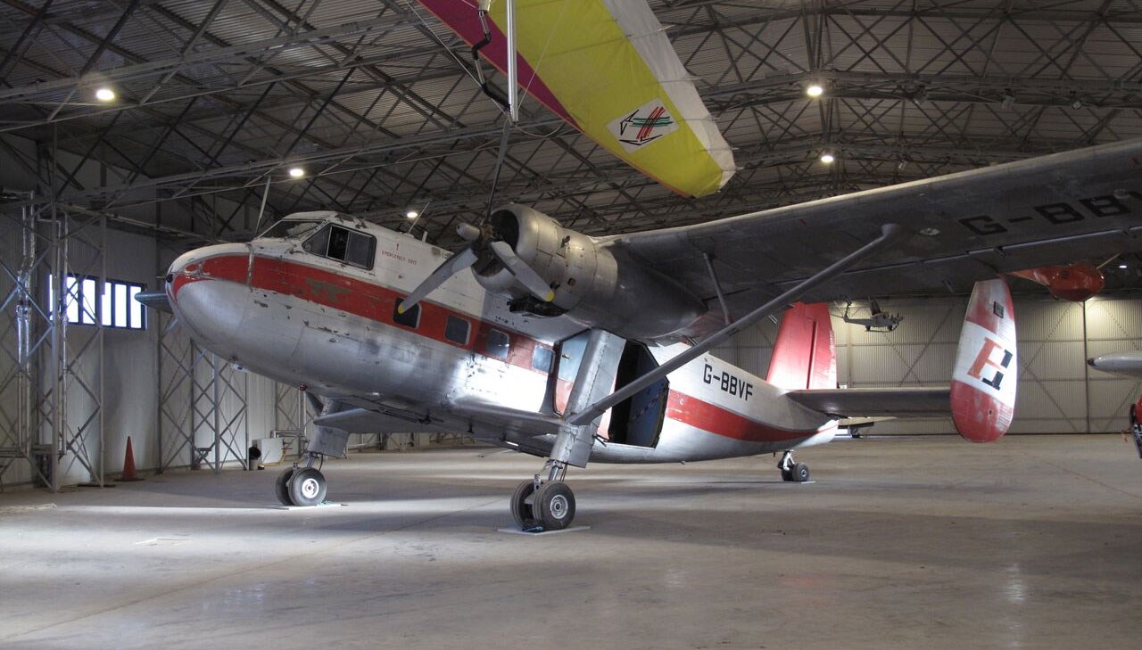 A white Scottish Aviation Twin Pioneer aircraft with a red stripe parked in a large hangar.