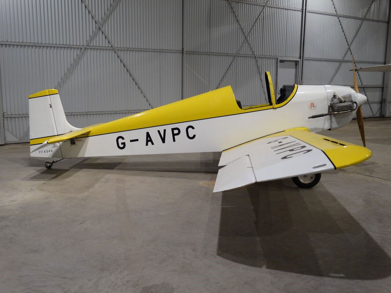 The side of a yellow and white Druine Turbulent aircraft inside a hangar.