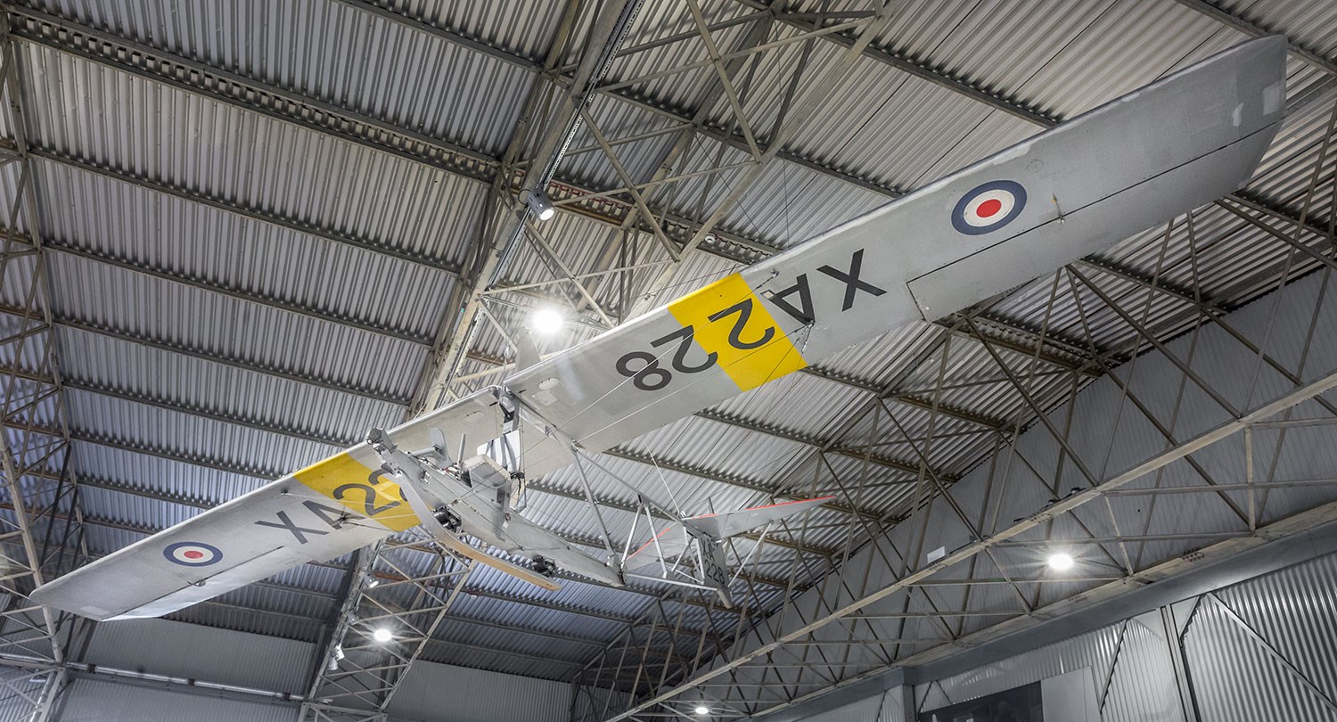 A grey Grasshopper aircraft with wide wings hanging from the ceiling of a hangar.