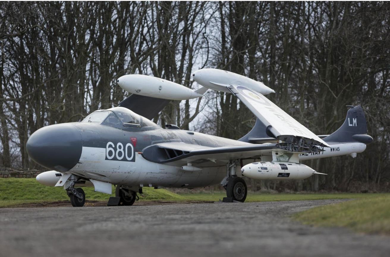 A grey de Havilland Sea Venom aircraft parked on a runway. Its wings are folded.