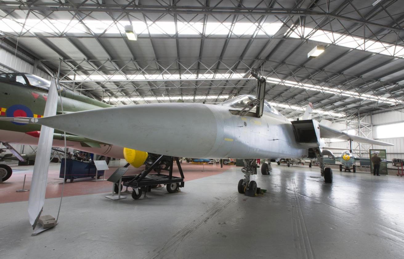 A grey Panavia Tornado aircraft with a long pointed nose parked in a large avaition hangar.