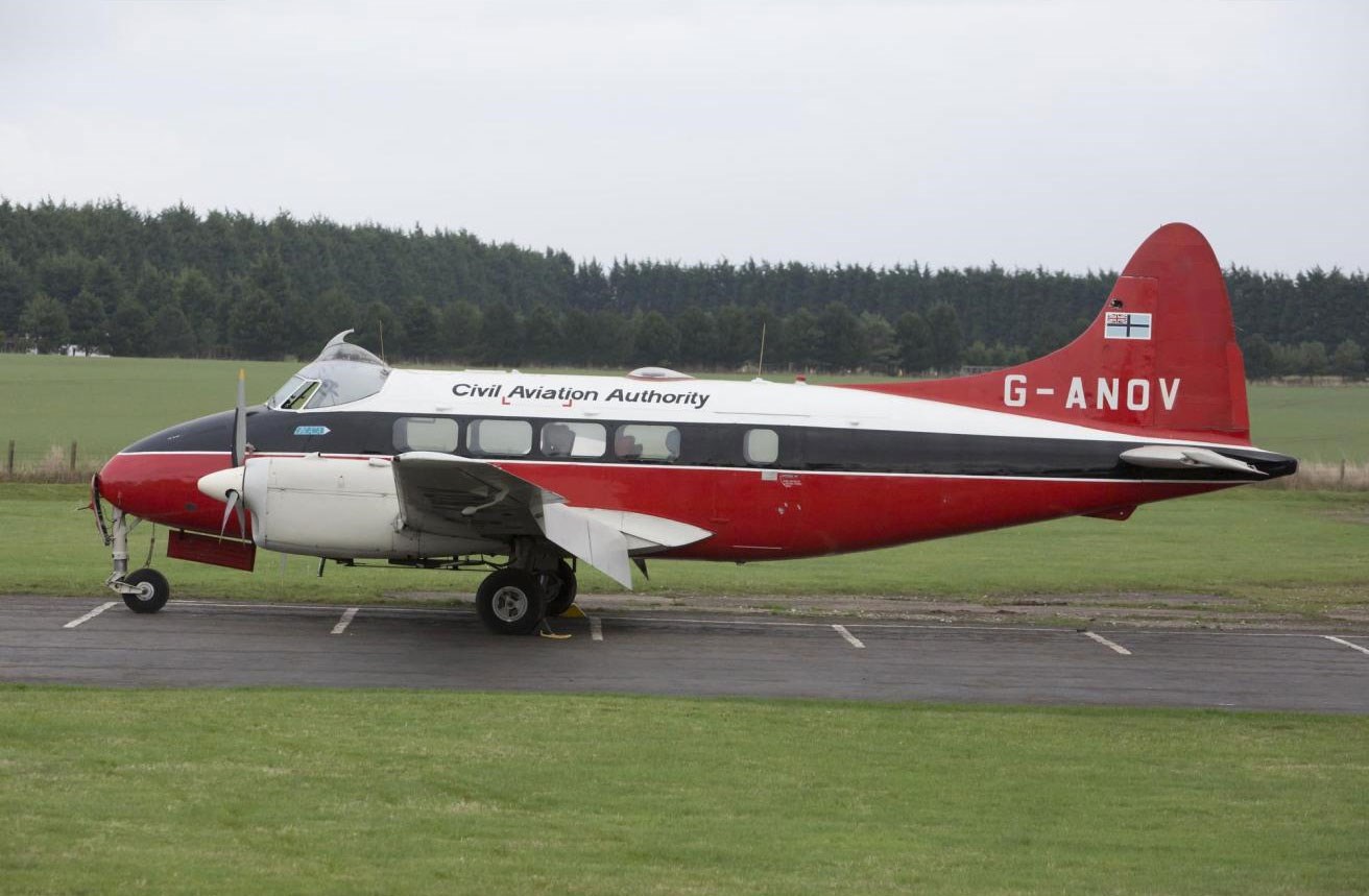 A red, white, and black de Havilland Dove aircraft on a runway.