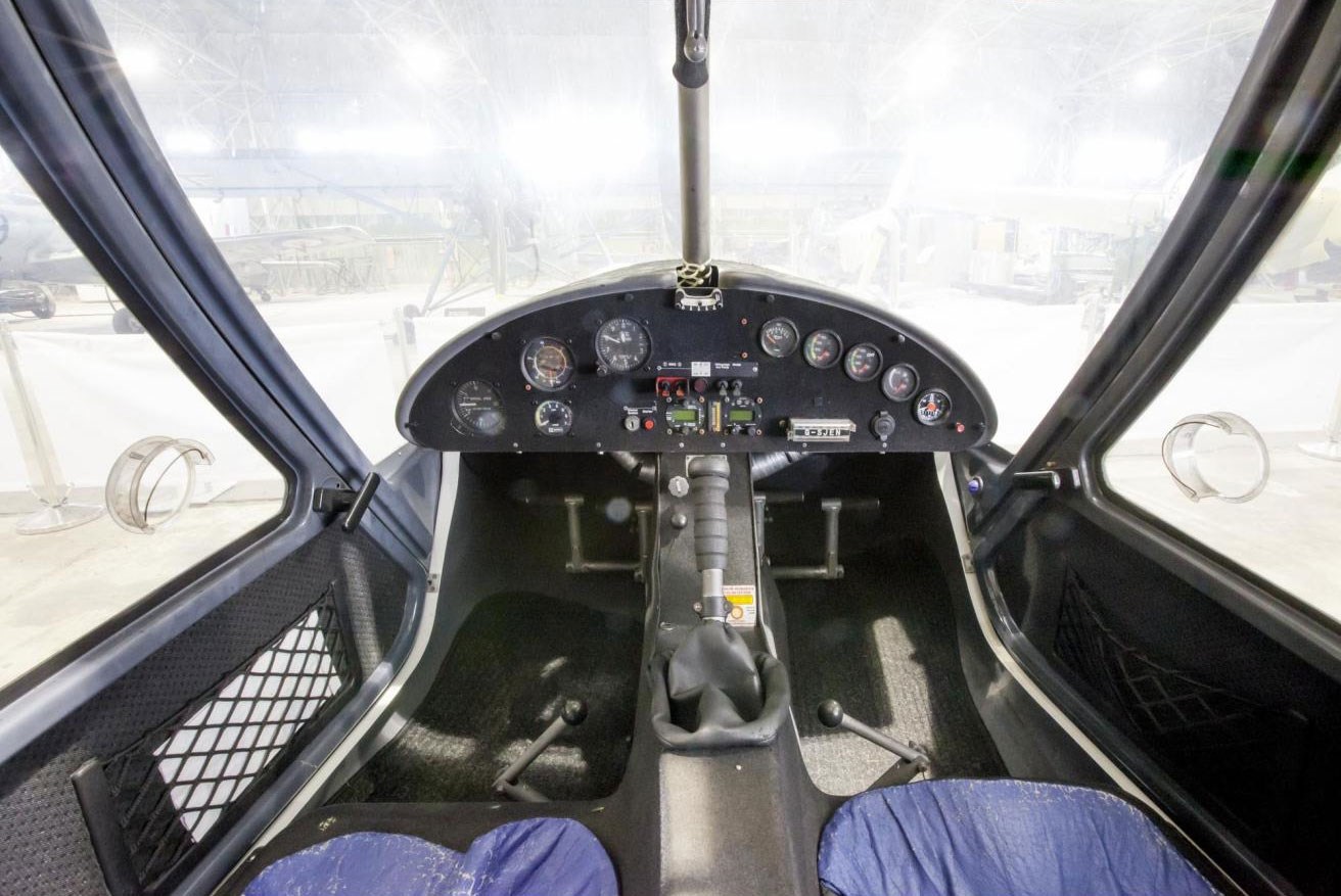 Inside the cockpit of an Ikarus aircraft. There are blue padded seats and several dials and buttons on the dashboard.