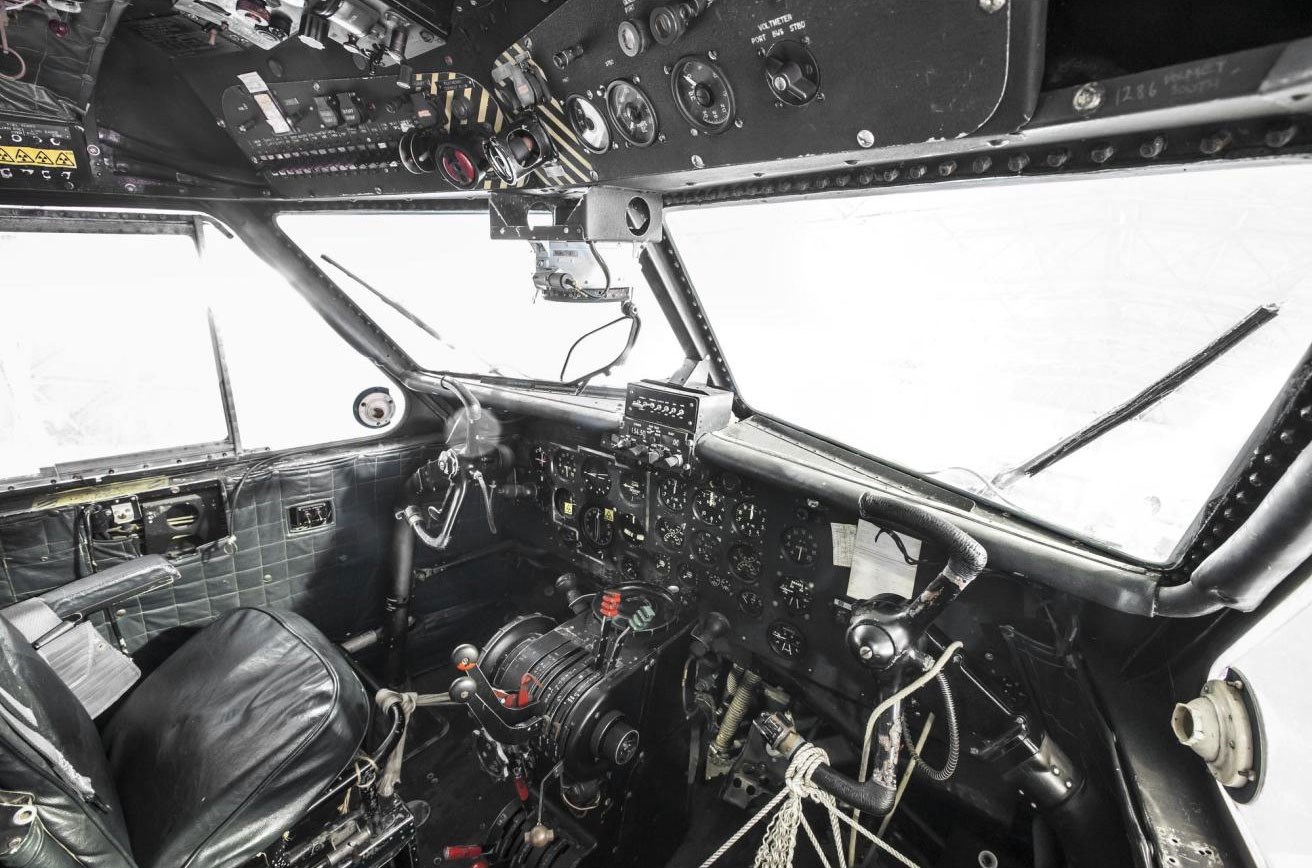 Inside the cockpit of a Twin Pioneer aircraft. There is a black padded seat and several dials and buttons.