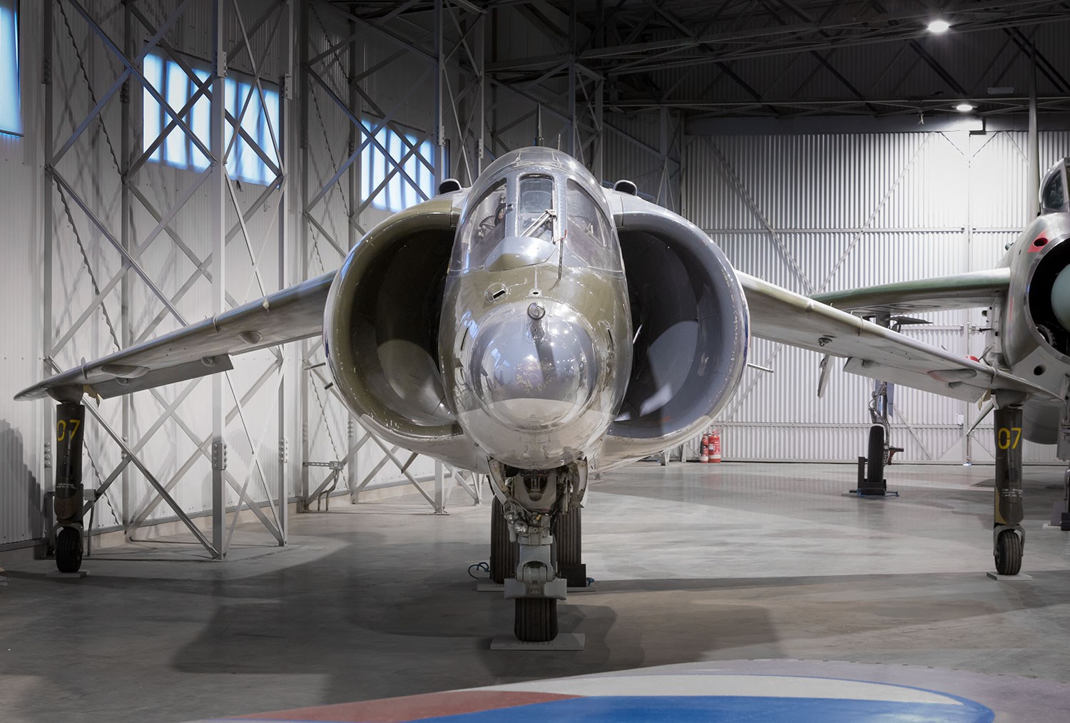 The front of a Hawker Harrier aircraft parked in a large hangar.