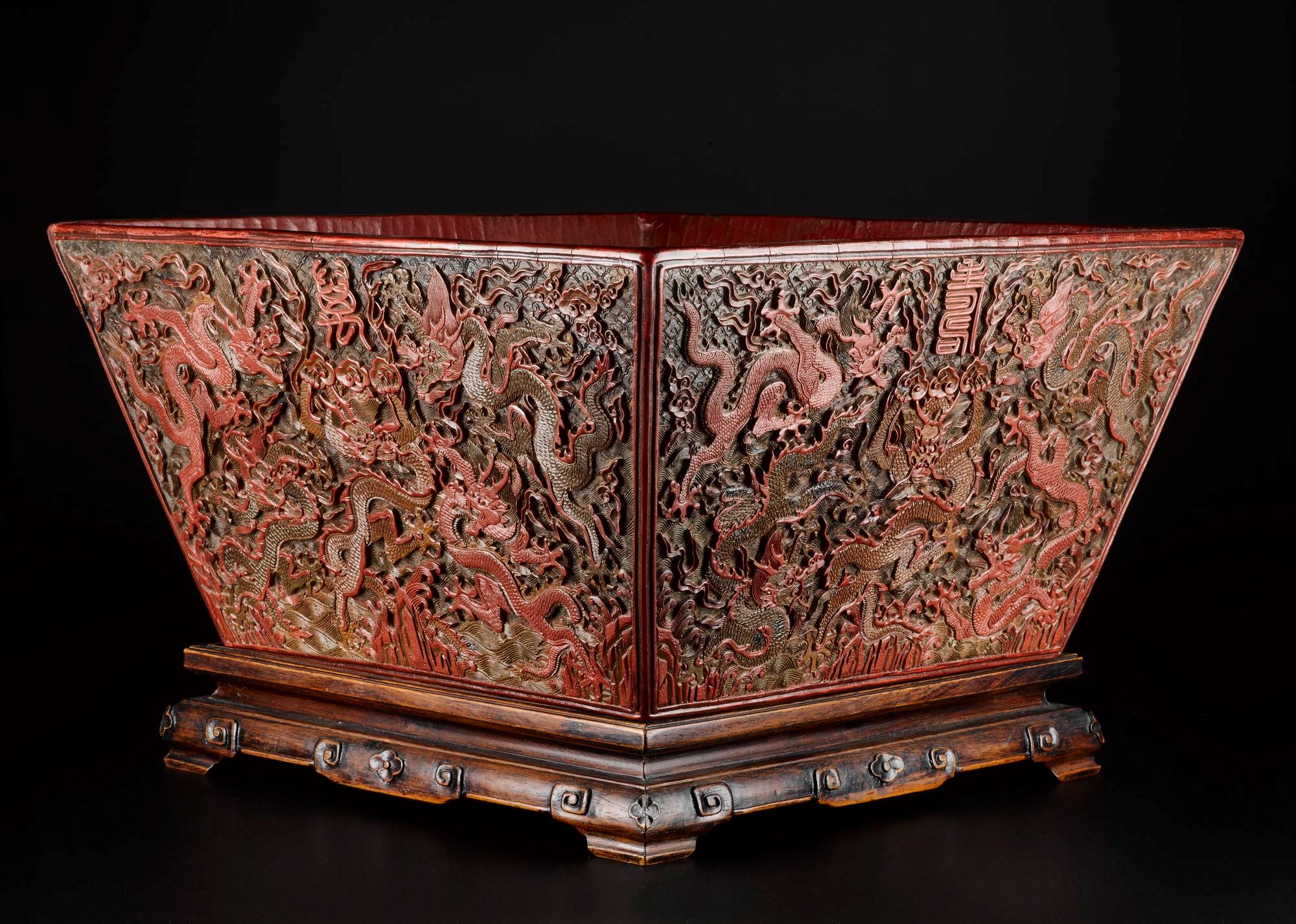 Rice measure of carved red, green and brown lacquer, square and decorated with five-clawed dragons in clouds above mountains and sea, with reign mark on base, and with wooden stand: China, Ming Dynasty, Jiajing reign, 1521-1567 AD.