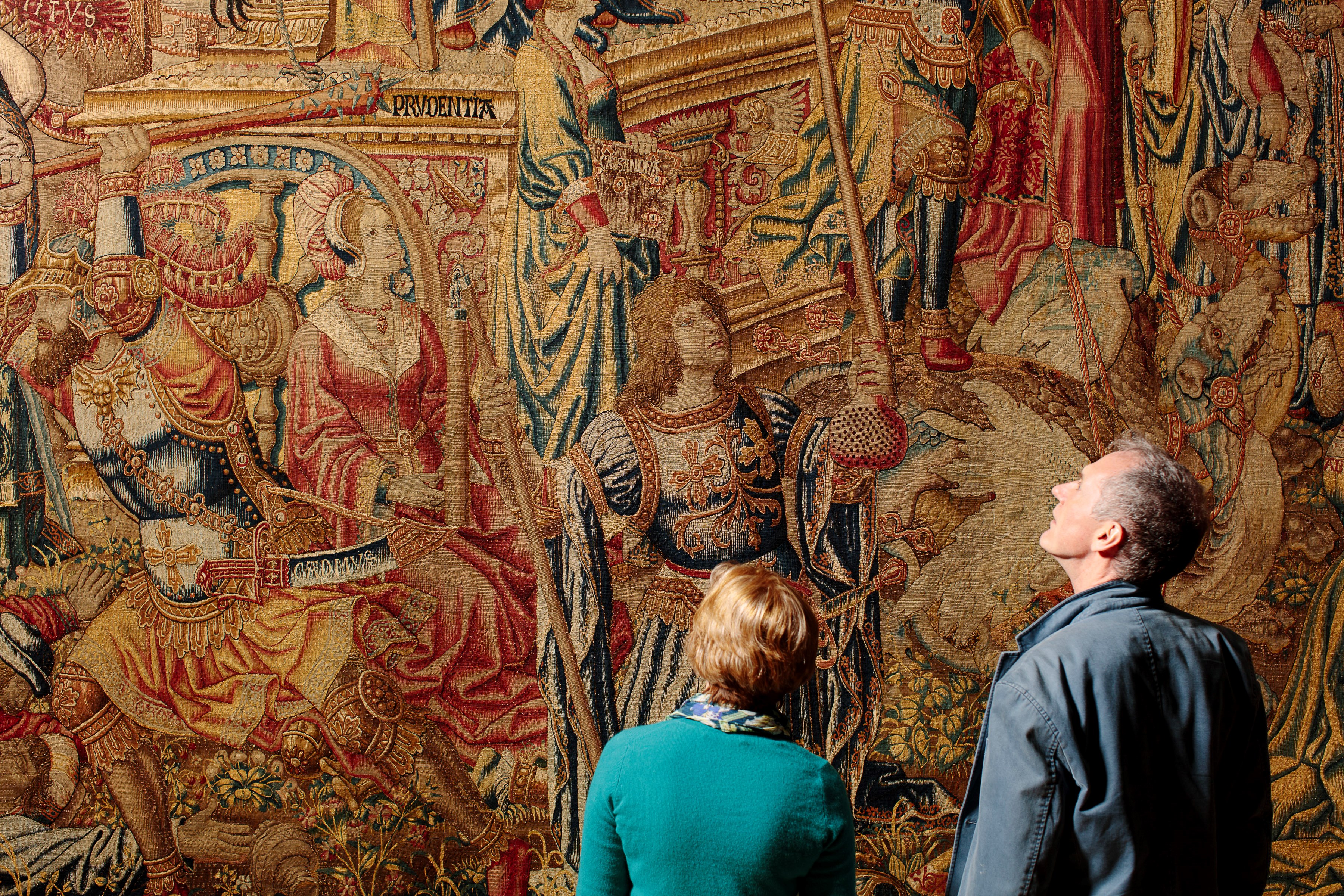 Two visitors look at a large tapestry hanging on a wall.