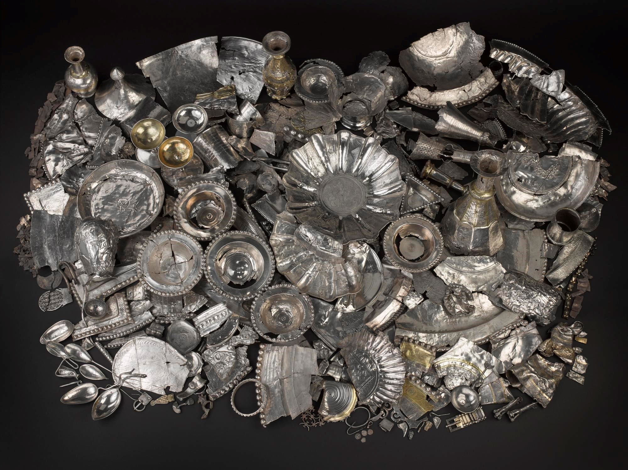 A huge pile of silver objects on a black background, from plates and vessels to tiny fragments and a large bowl in the centre.