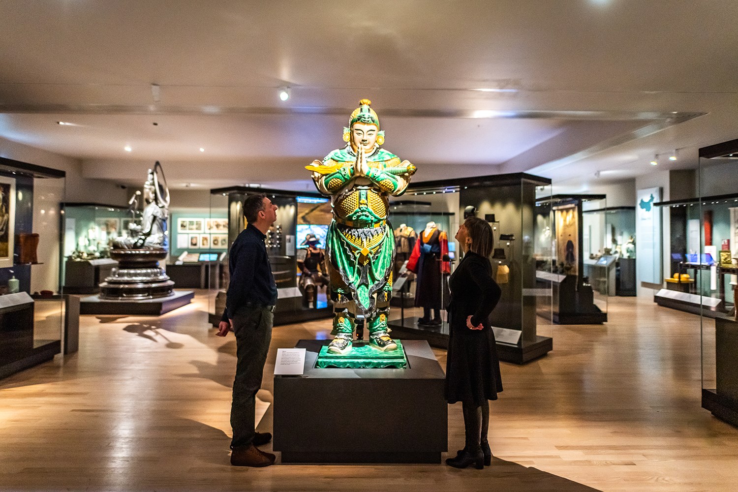 Two people in a gallery looking up at the figure of the bodhisattva Weituo in the East Asia gallery.