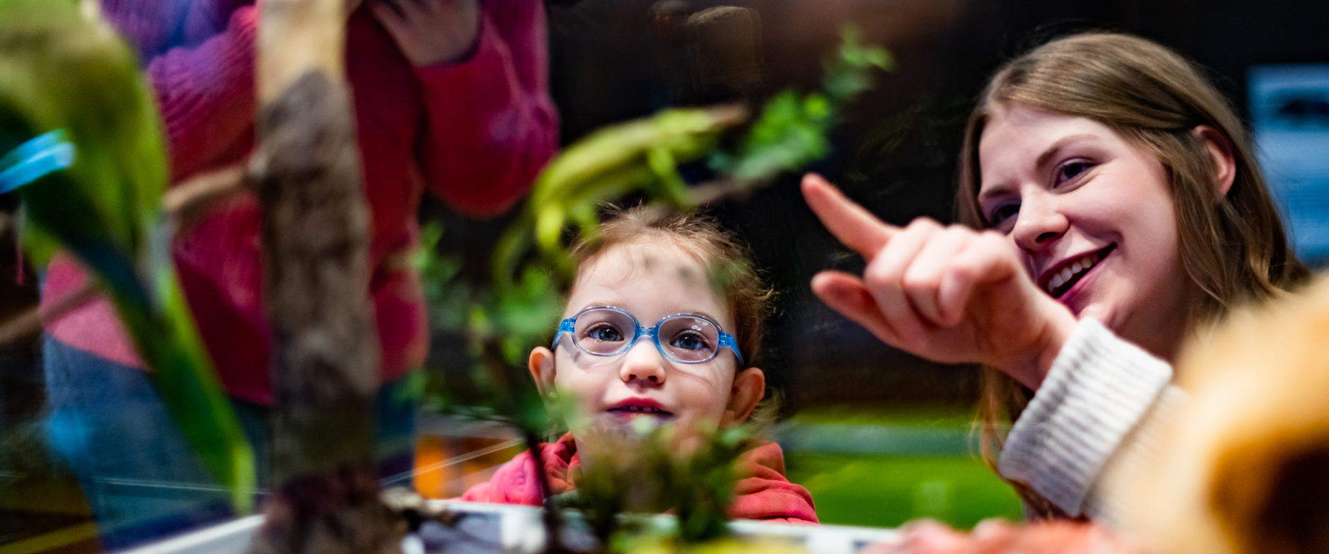 A child looks as a woman points at something out of focus in a glass case.