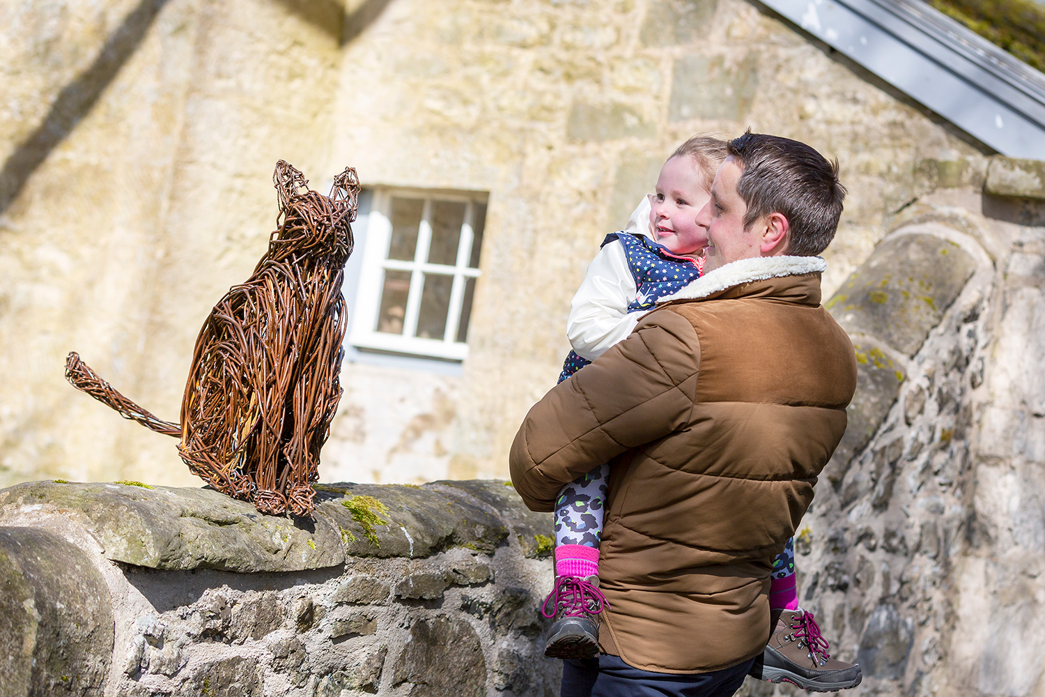 Visitors look at a willow sculpture of a cat sitting on a wall
