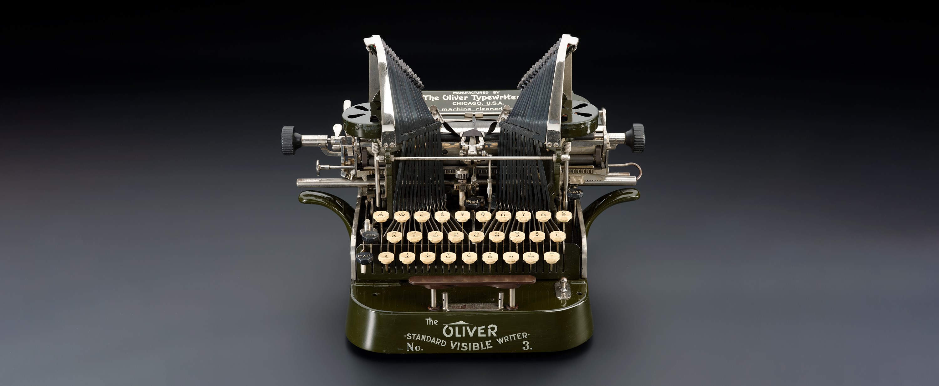 Green mechanical typewriter from the early 1900s with white keys. It says 'The Oliver No. 3, Standard Visible Writer' on the front.