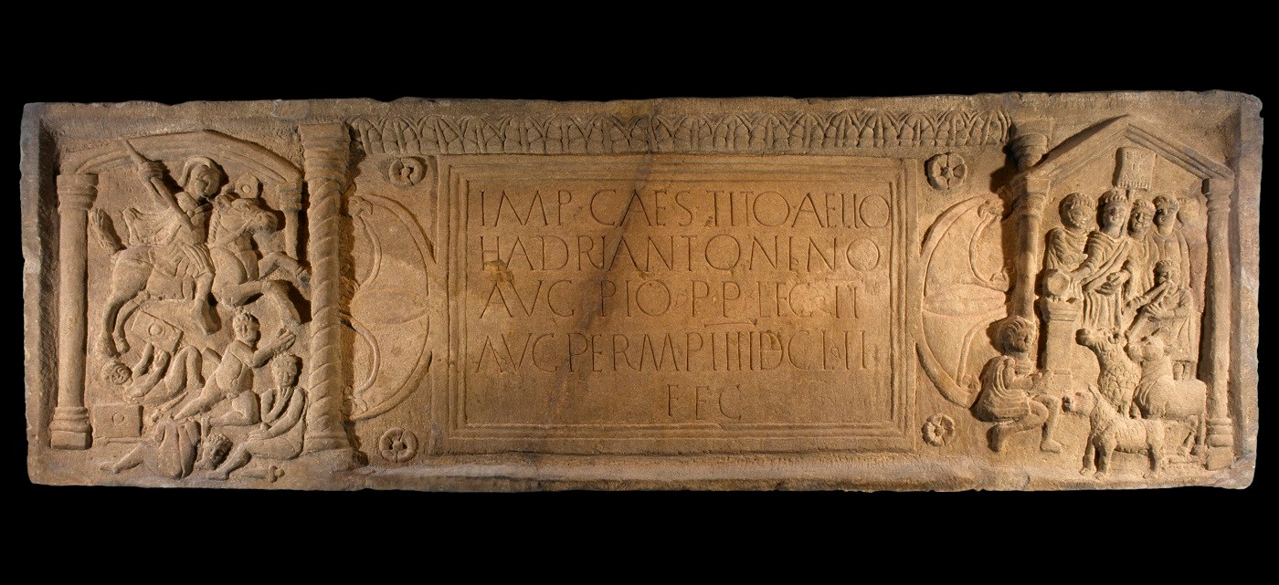 Large, rectangular slab with a central inscription flanked by deeply-carved engravings of cavalry, civilians with livestock and columns.