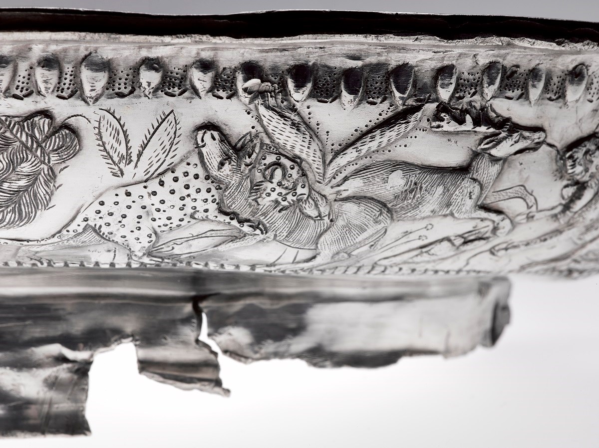 Close-up of an engraves scene on a dish depicting a leopard or lioness catching a deer while another deer runs away.