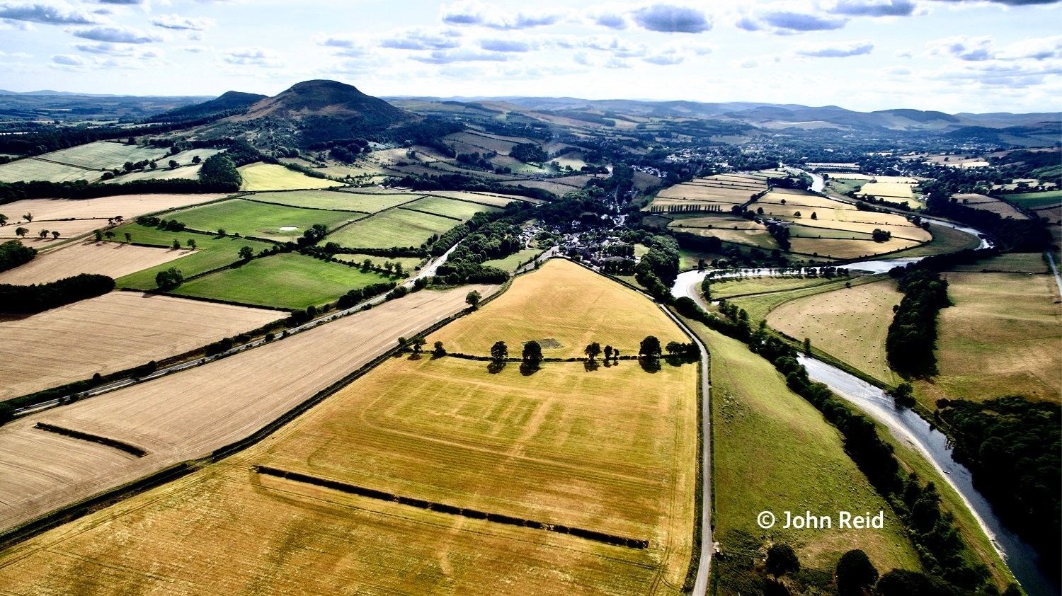Scenic aerial image of the River Tweed and Eildon Hills on a sunny day, with crop marks from the Roman fort visible in the foreground.