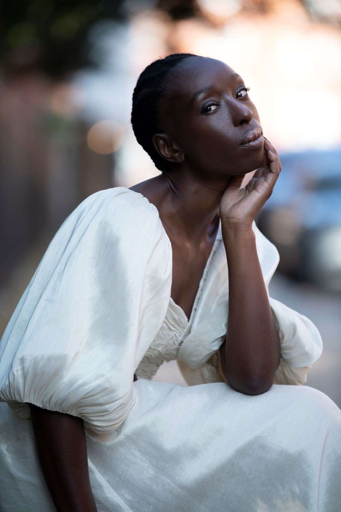 Portrait of Eunice Olumide, crouching down posing in a white dress 