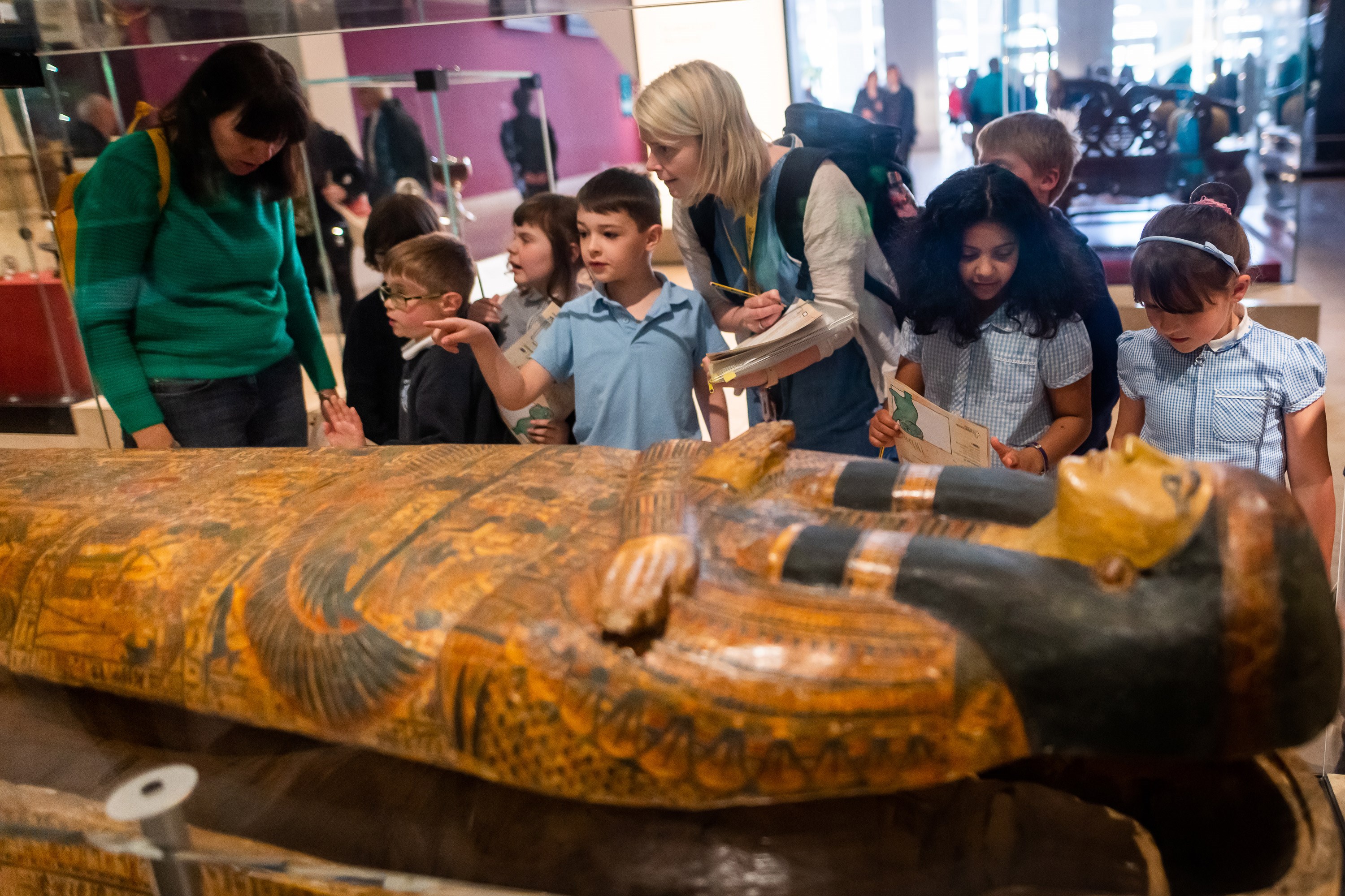 A teacher gathers a group of primary school pupils around an Egyptian Coffin. 
