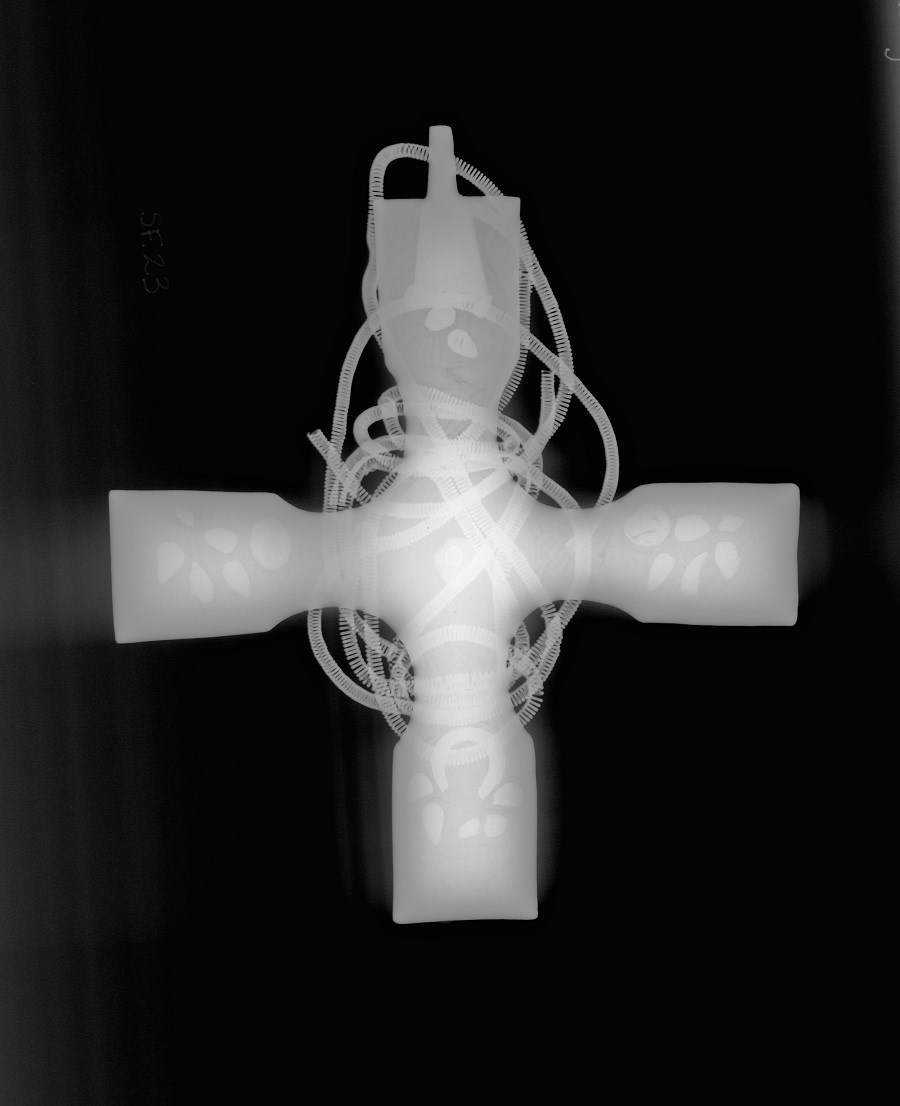 X-ray image of a cross rendered in silvery-white on a black background. The chain is bright white, with white patches at each terminus.