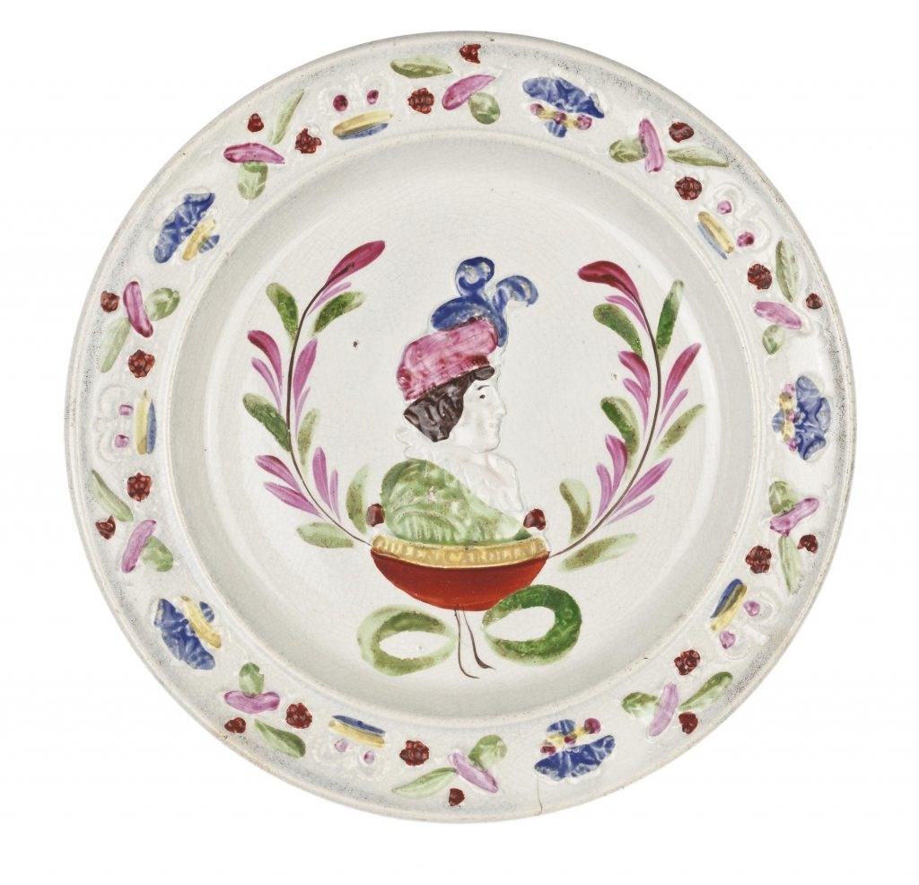 White earthenware plate with bust of a woman in a green dress and large pink hat surrounded by flowers.