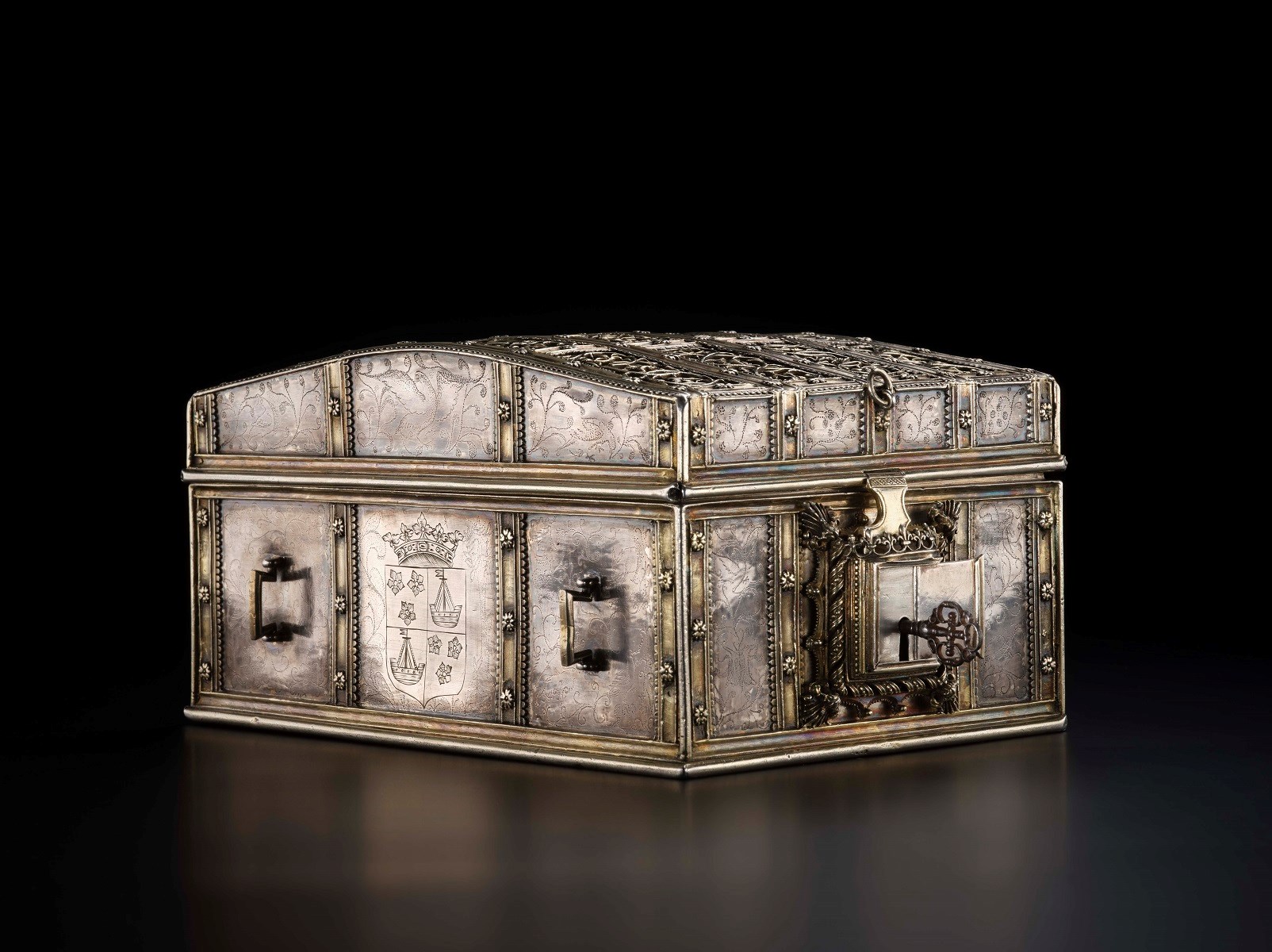 Ornate silver chest pointed at diagonally to view two sides at once. A heavy lock guards it and a coat of arms is inscribed on one side.