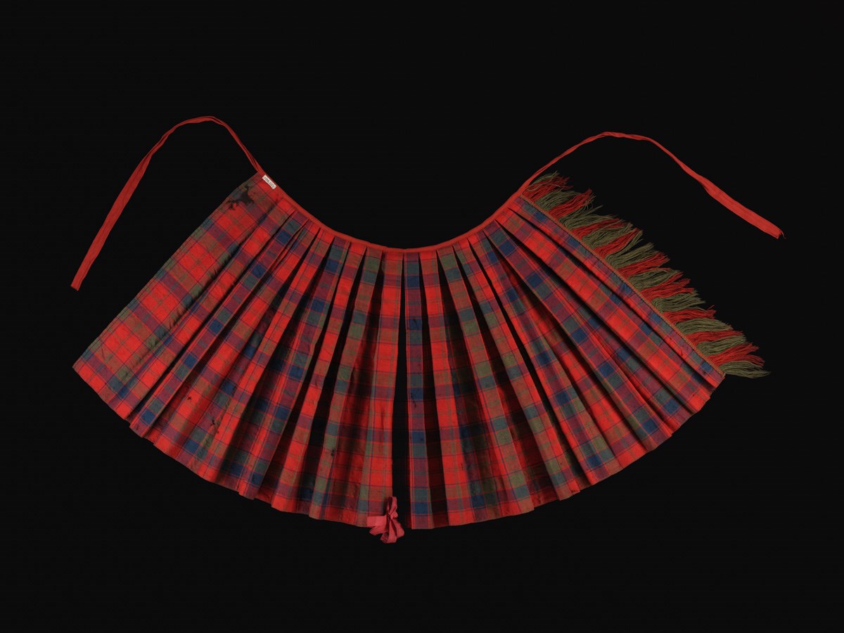 Pleated arc of red and green checkered tartan with strands at both top corners against a black background.