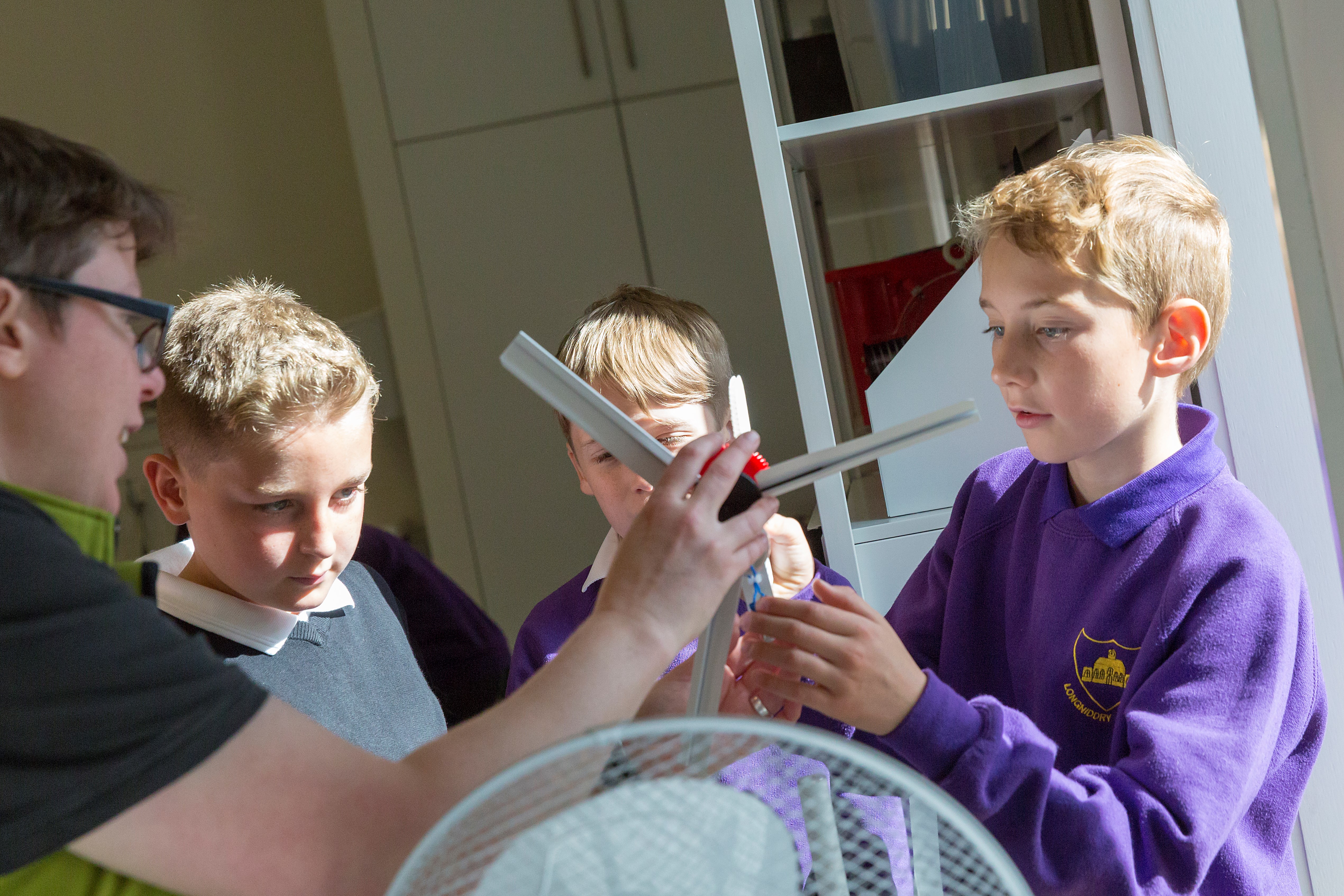 a learning enabler helps a group of primary pupils test their model wind turbine in front of a fan. 