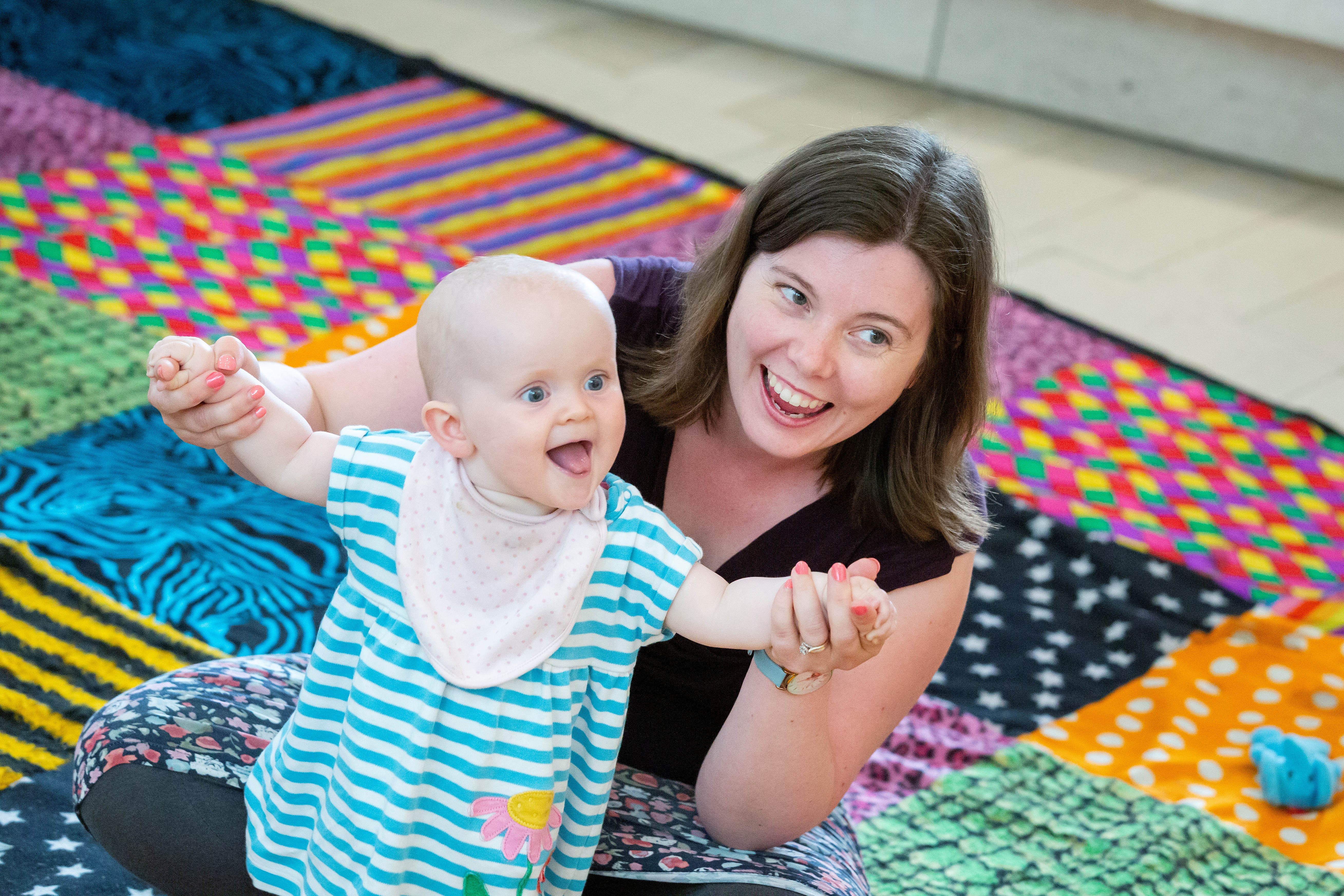 Woman and baby in arms sitting on the floor on a checked carpet.