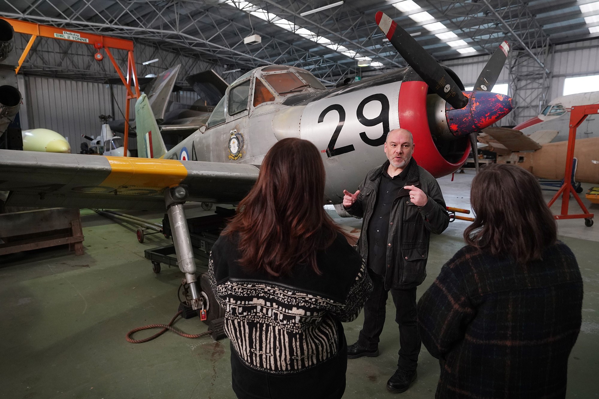Two visitors listening to a man talking in front of an aircraft.