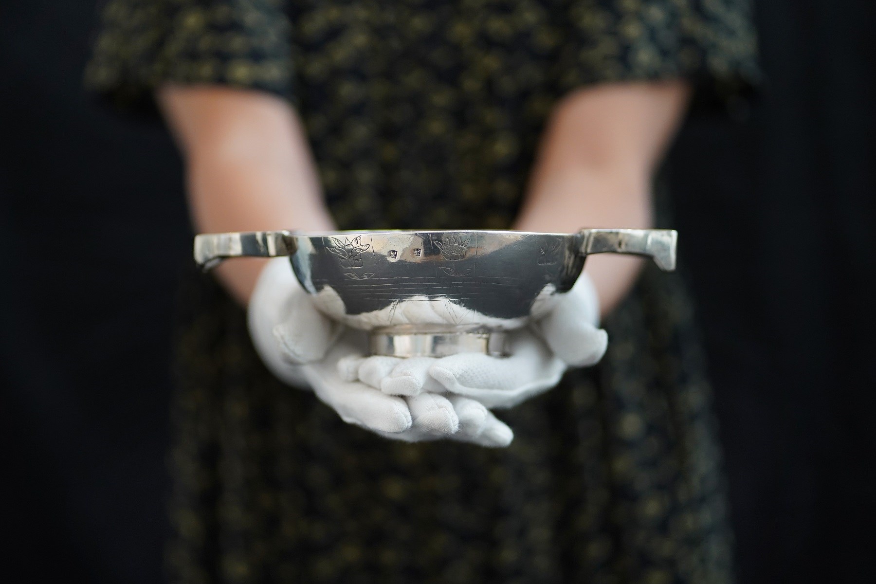 Closeup of a silver quaich being cradled in a woman's white-gloved hands.