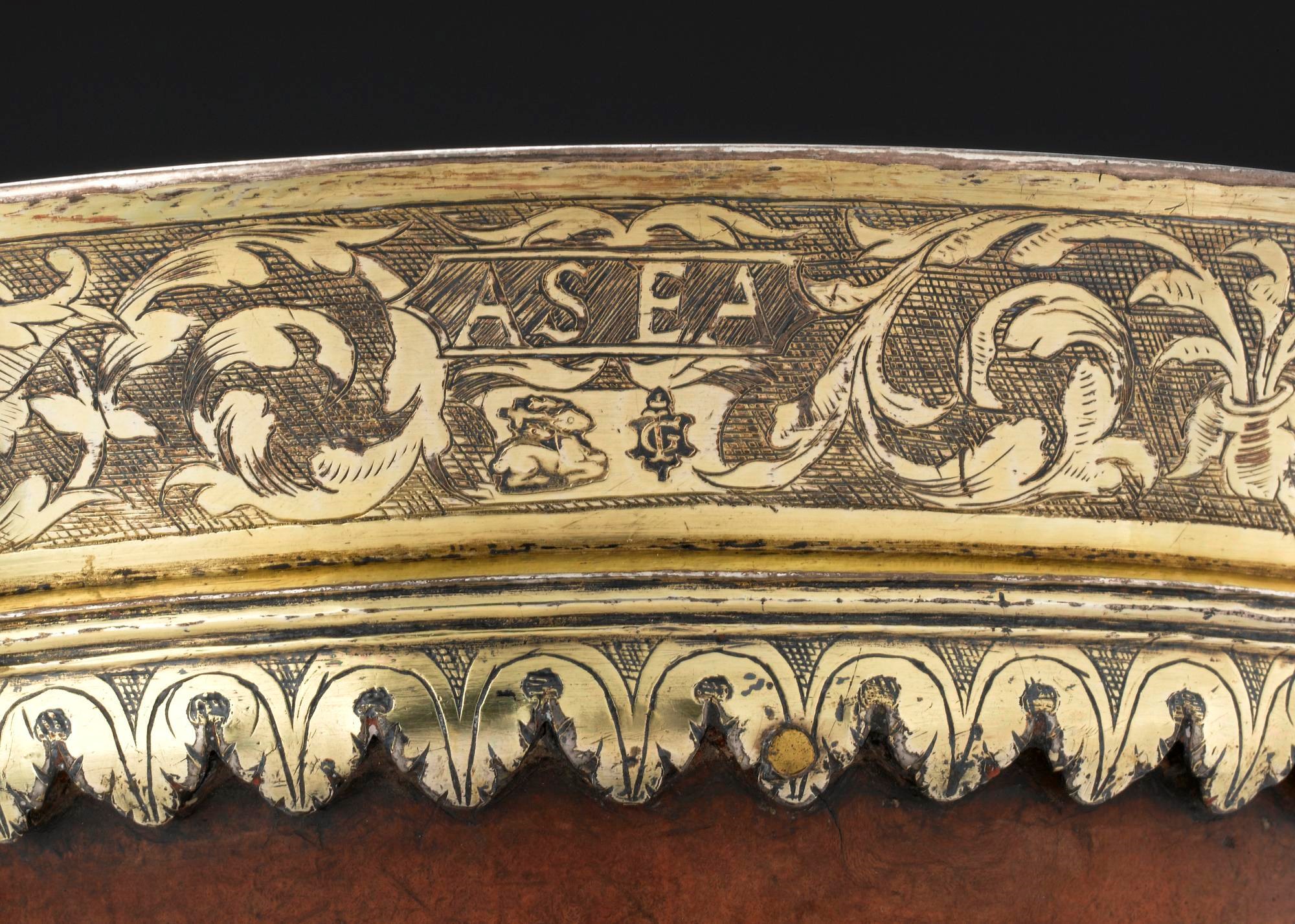 Closeup of the rim of the mazer, made from gold-coloured silver. The metal is engraved with the initials 'AS' and 'EA', and flanked by floral patterns.