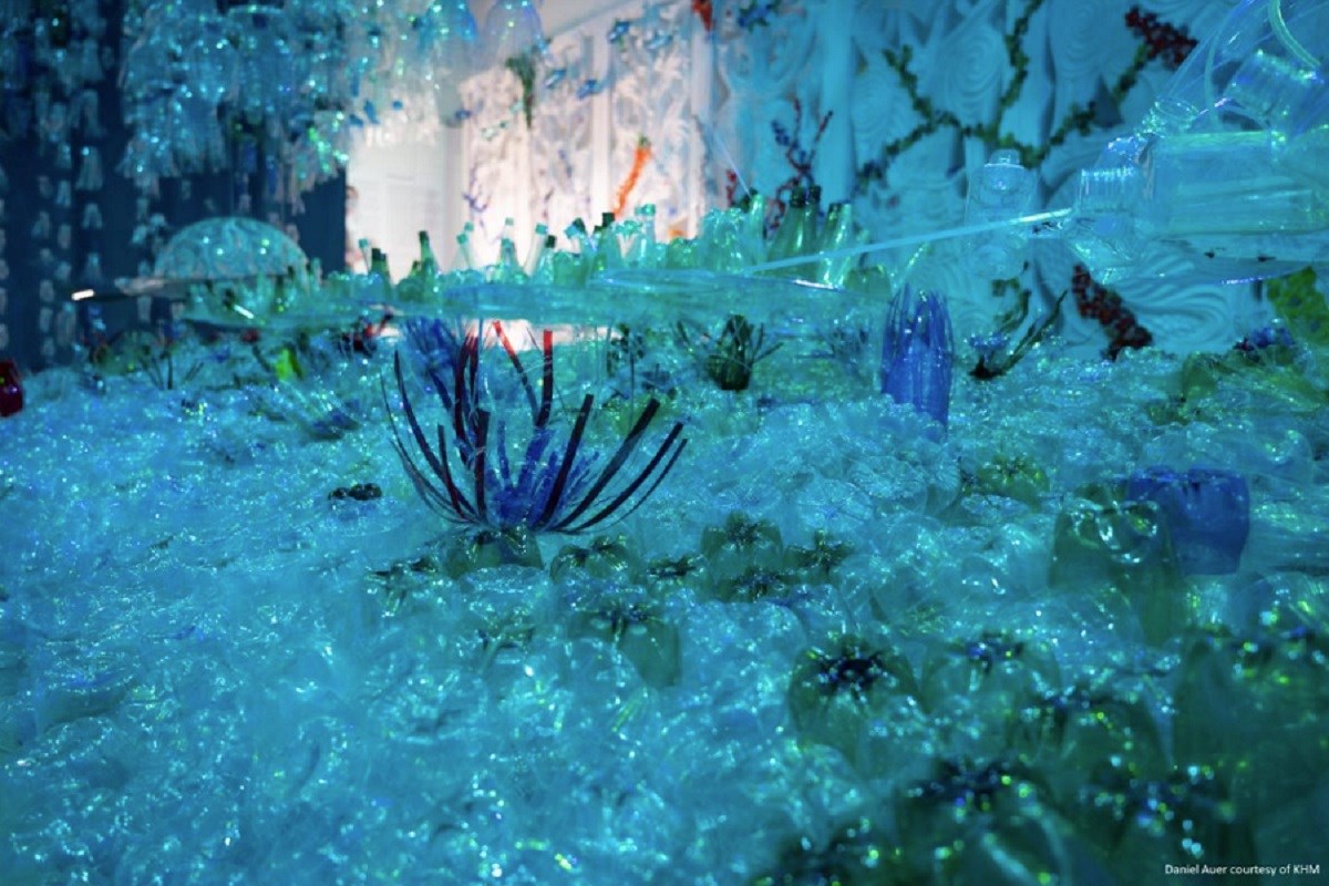 A museum display replicating a vibrant, bright blue sea floor, but with everything made from plastic - plastic bottle jellyfish, plastic padding on the floor, and plastic straws forming anemones.