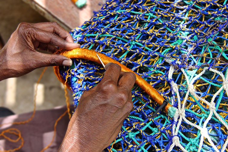 Closeup of a person's hands working on a blue and green net made of recycled plastic.