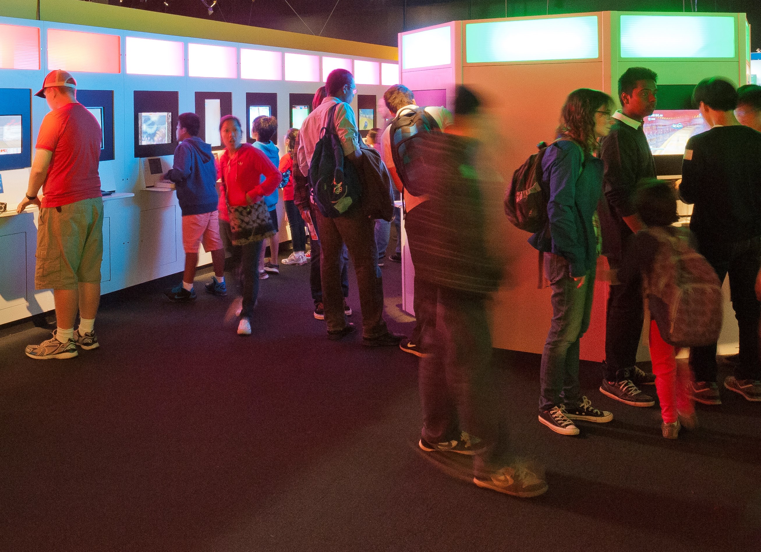 Ten players crowd around a line of consoles in an exhibition space at Game On in Ontario Science Centre.ario Science Ce