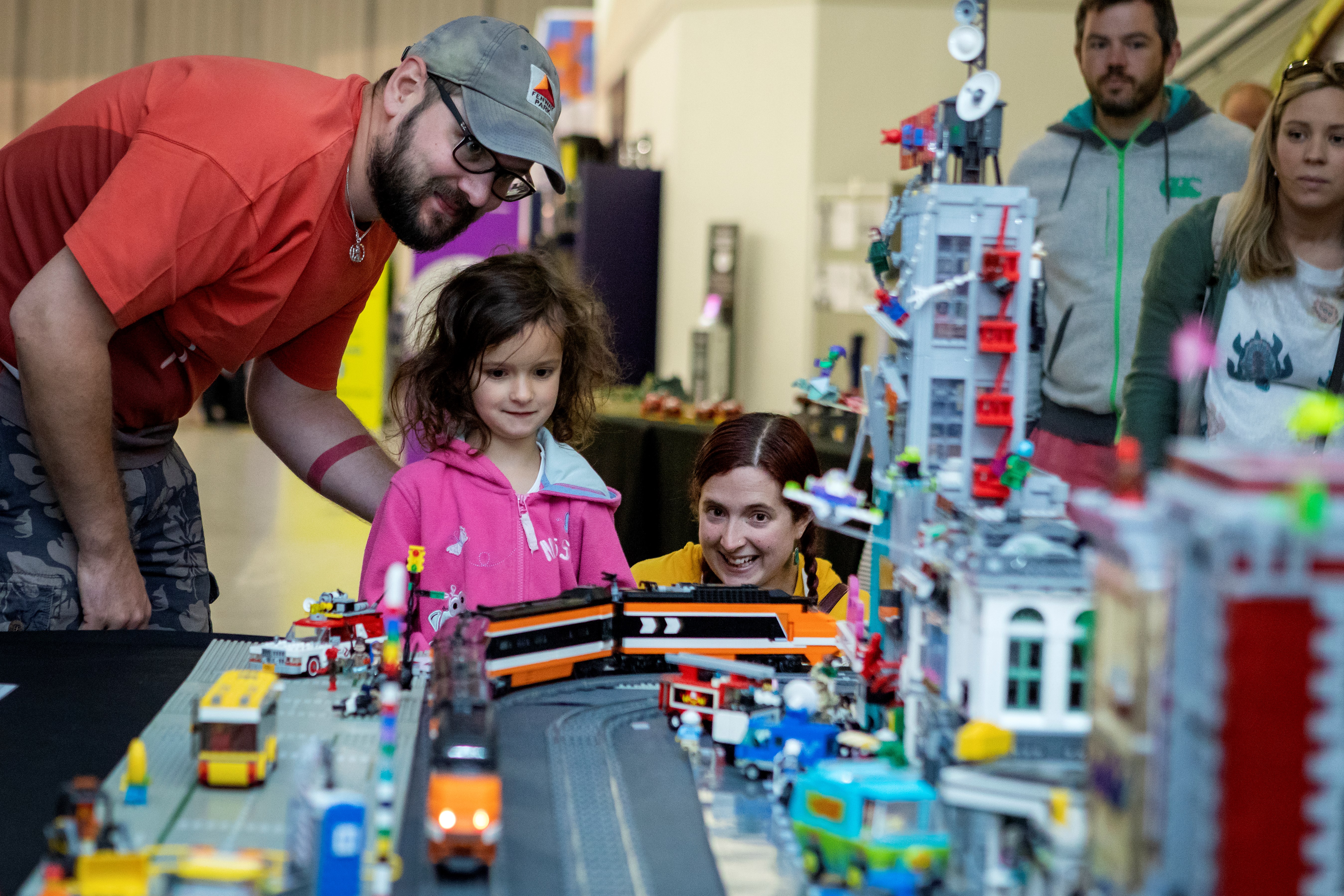 Two adults and a child look at Lego models on a table.