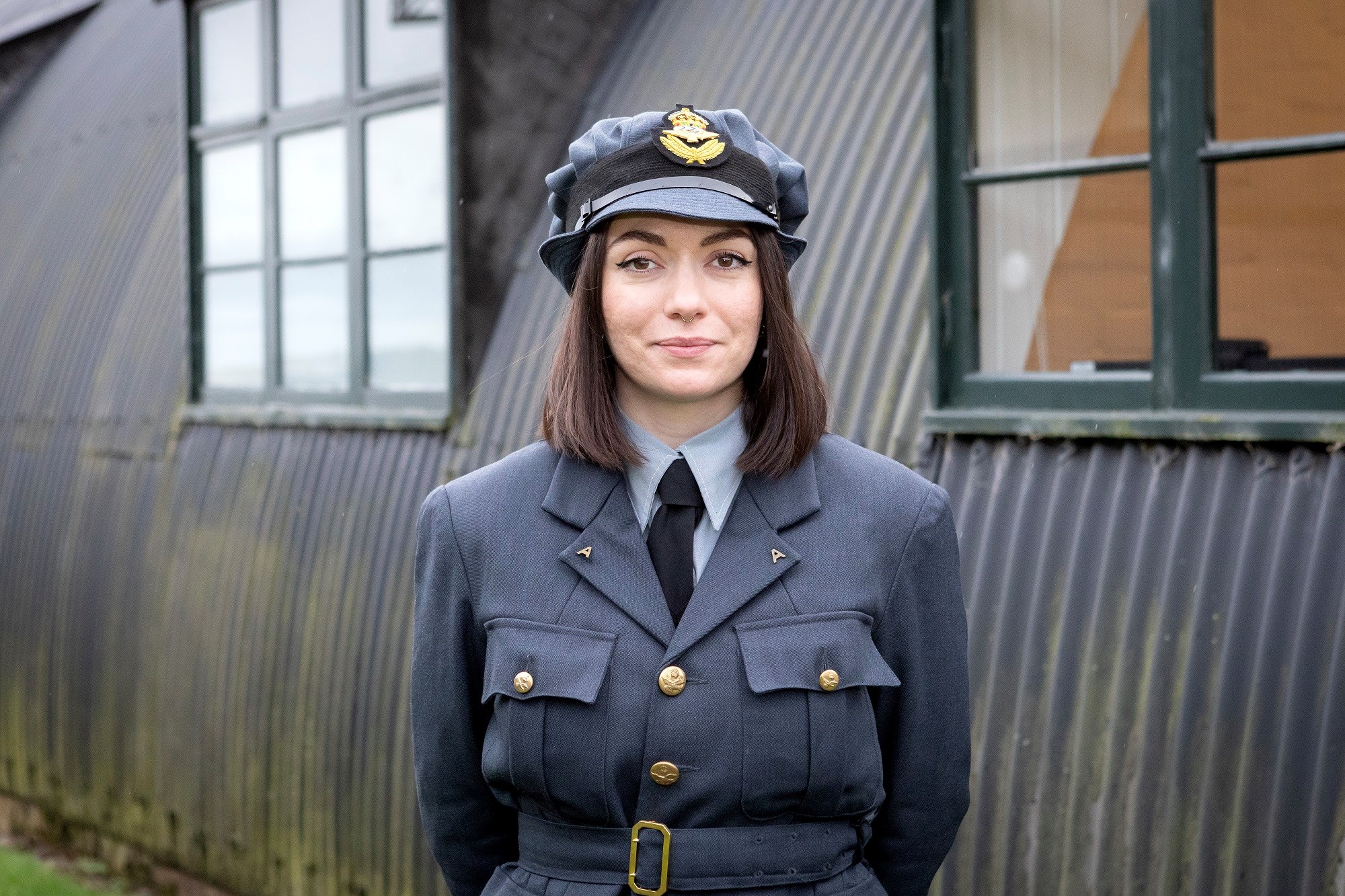 A woman in a blue RAF uniform is looking directly at the camera, outside at the National Museum of Flight.