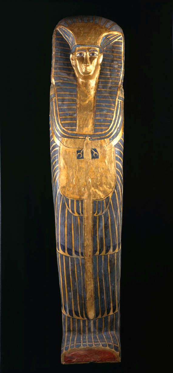 Female coffin: an exceptionally tall coffin with decoration in the rishi-style. The lid has feathered patterning painted in blue with black details on a yellow ground. The owner’s face is framed by a striped linen nemes-cloth, a beaded collar with falcon terminals, and a vulture-pectoral.