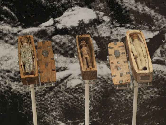 Three of the Arthur's Seat miniature coffins, all open to reveal the dolls. Propped up for display with background image of a rocky hillside.