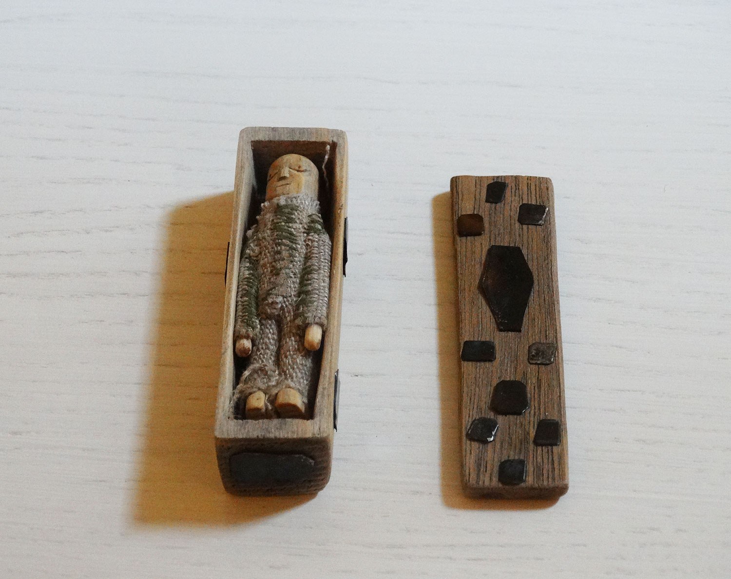 A small open wooden coffin with a doll dressed in a knitwear-like outfit inside.