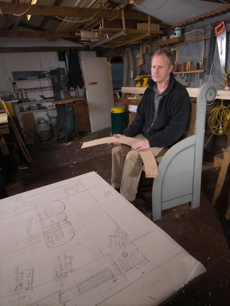 Furniture maker Adrian McCurdy sits on a model of the throne looking at drawings and plans for the final design