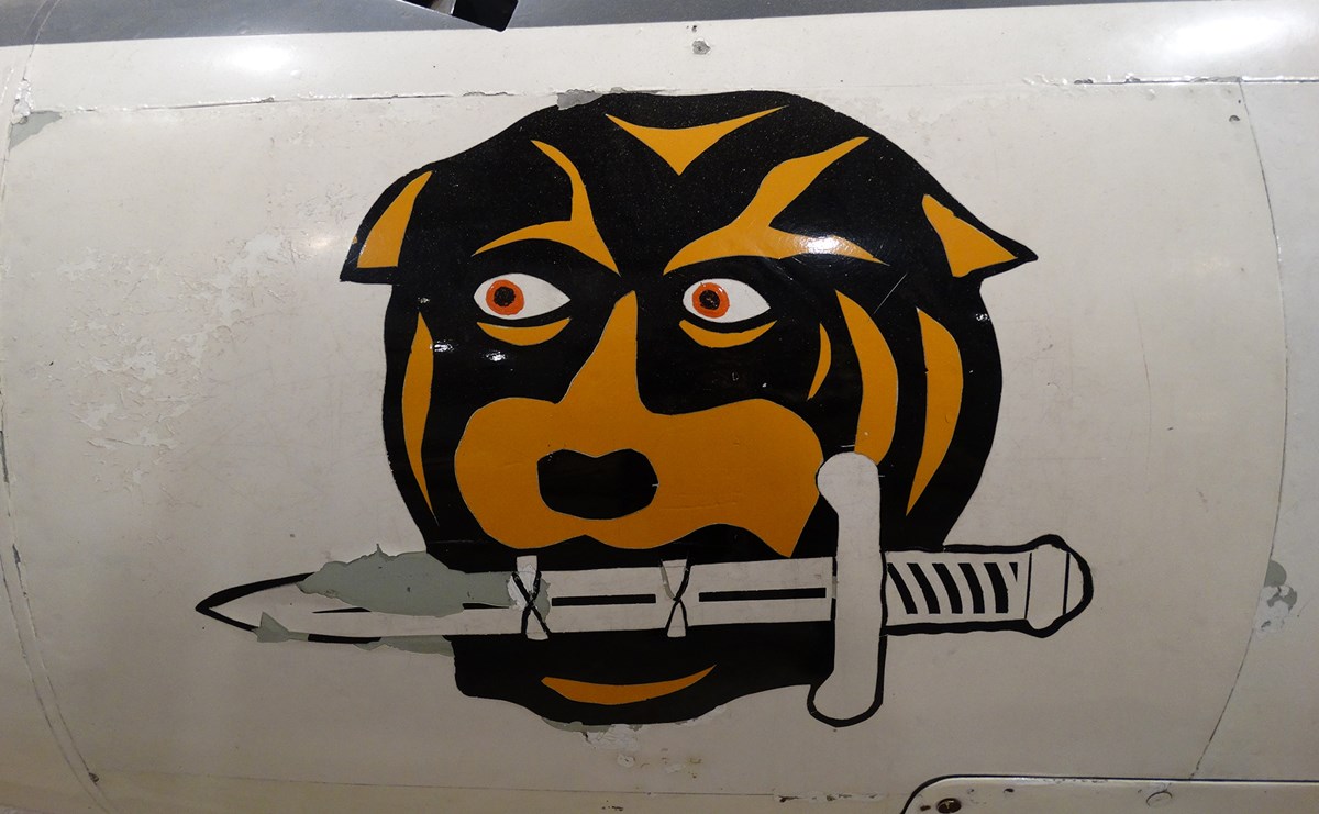 The side of a plane with a dog holding a knife in its mouth painted on it