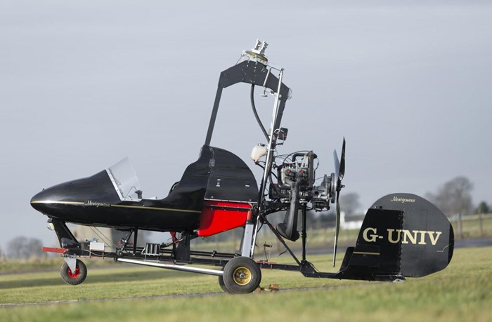 The sideview of a black Montgomerie-Parsons gyrocopter on a runway.