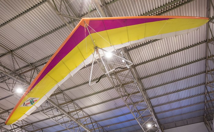 A colourful Airwave Magic Kiss hang-glider hanging from the ceiling of a hangar.