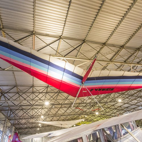A mutlicoloured hang glider suspended from the ceiling of a hangar at the National Museum of Flight.