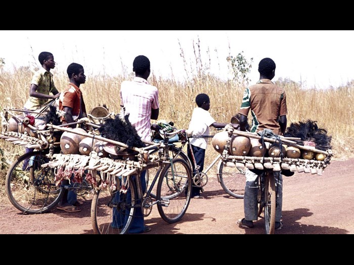 Slide of boys transporting drums and xylophones on the back of their bicycles: Nawalakaha, Ivory Coast, 1977, photographed by Jean Jenkins.